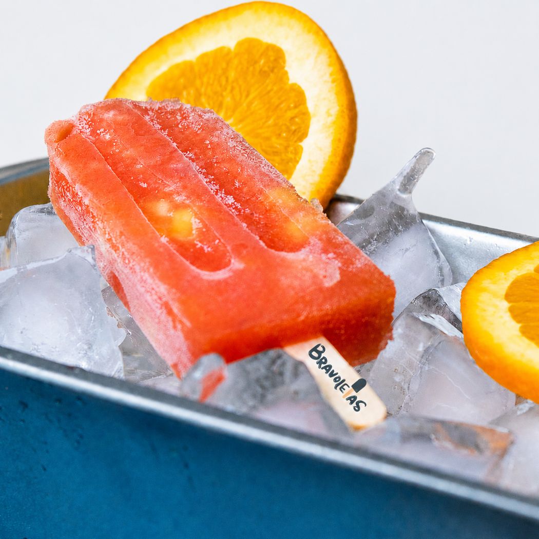 Paleta artesanal de frutas mixtas sobre hielo y rodaja de naranja